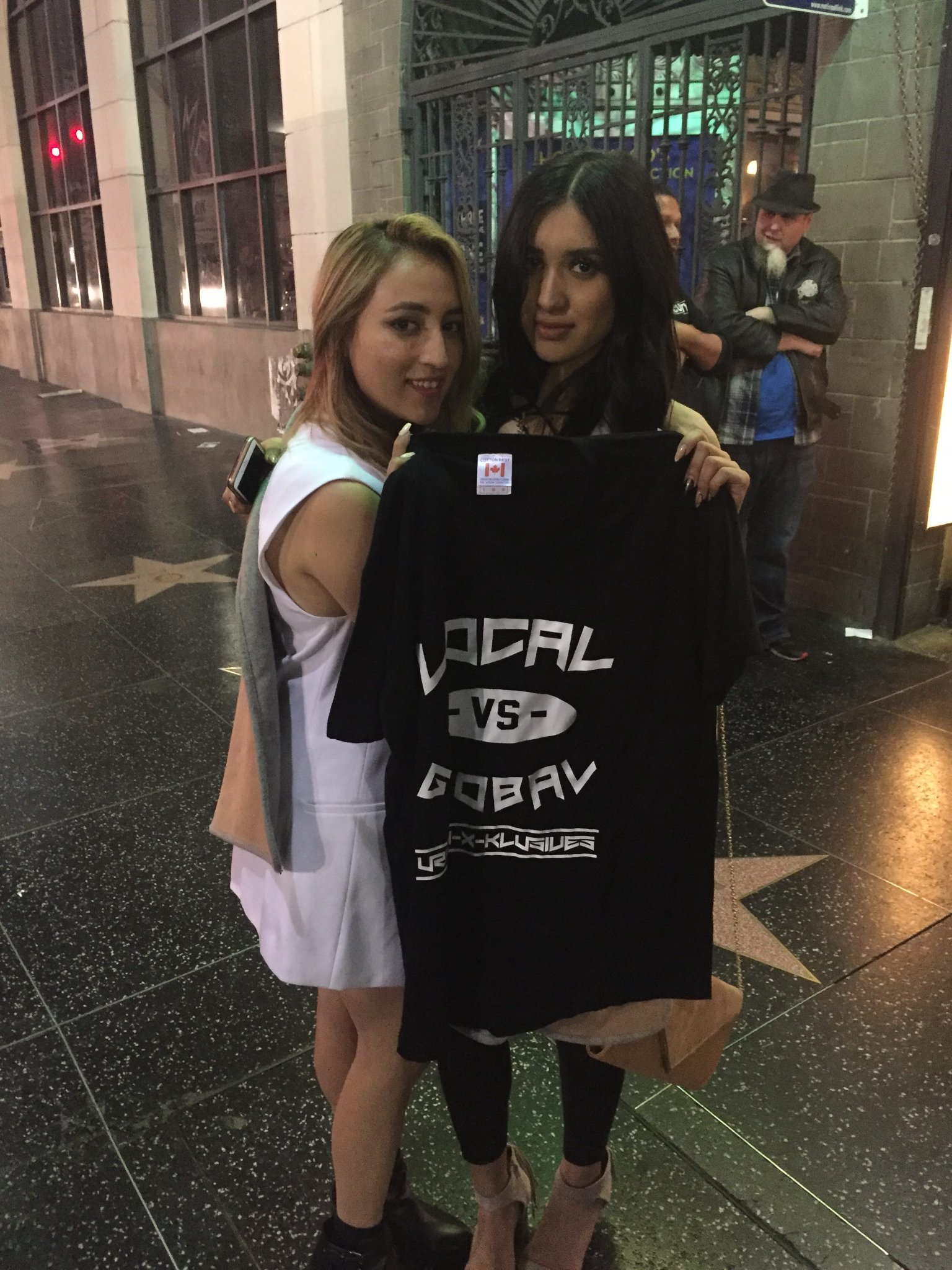 Two women on Hollywood Boulevard holding up a UXK Local vs Global shirt